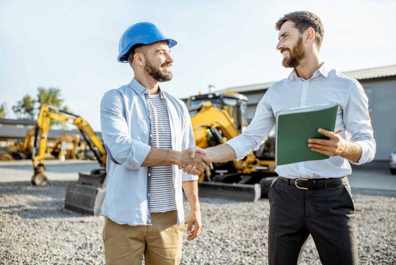 Zwei Männer auf Baustelle schütteln nicht sich Hand und unterhalten sich über die digitale Baustelle
